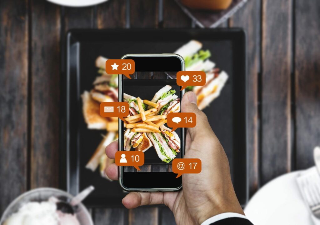 una mano tiene uno smartphone con aperta una app social media con icone di messaggi, video, likes ecc.