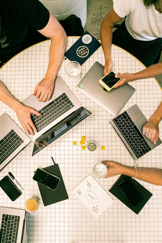 3 persone sono sedute a una tavola rotonda con smartphone e computer portatili per discutere una strategia di Social Media Marketing.