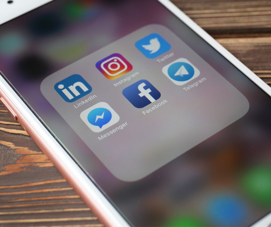 Sullo schermo di un cellulare appoggiato a un tavolo di legno compaiono le icone di Facebook, Instagram, LinkedIn e Twitter